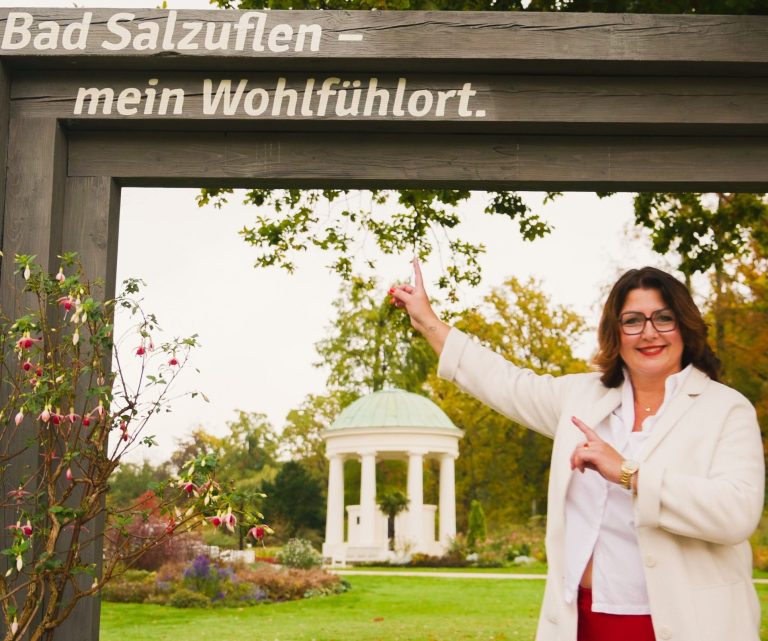 Immobilienmaklerin Sandra Kiefer im Kurpark Maklerin von Kiefer Immobilien im Kurpark Bad Salzuflen, Sandra Kiefer, im Kurpark vor Aufschrift "Bad Salzuflen - mein Wohlfühlort"